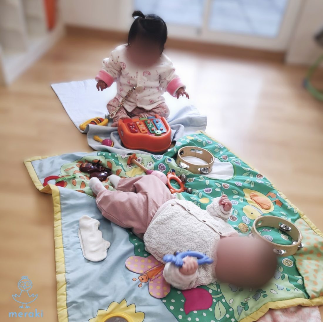 Dos bebés del aula de Cargolins jugando en el suelo, sobre una manta, rodeados de instrumentos musicales y materiales sensoriales
